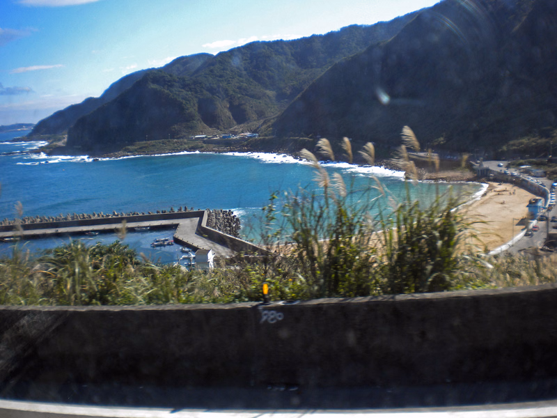 A view of a curved sandy beach nestled between lush green mountains and the blue ocean.