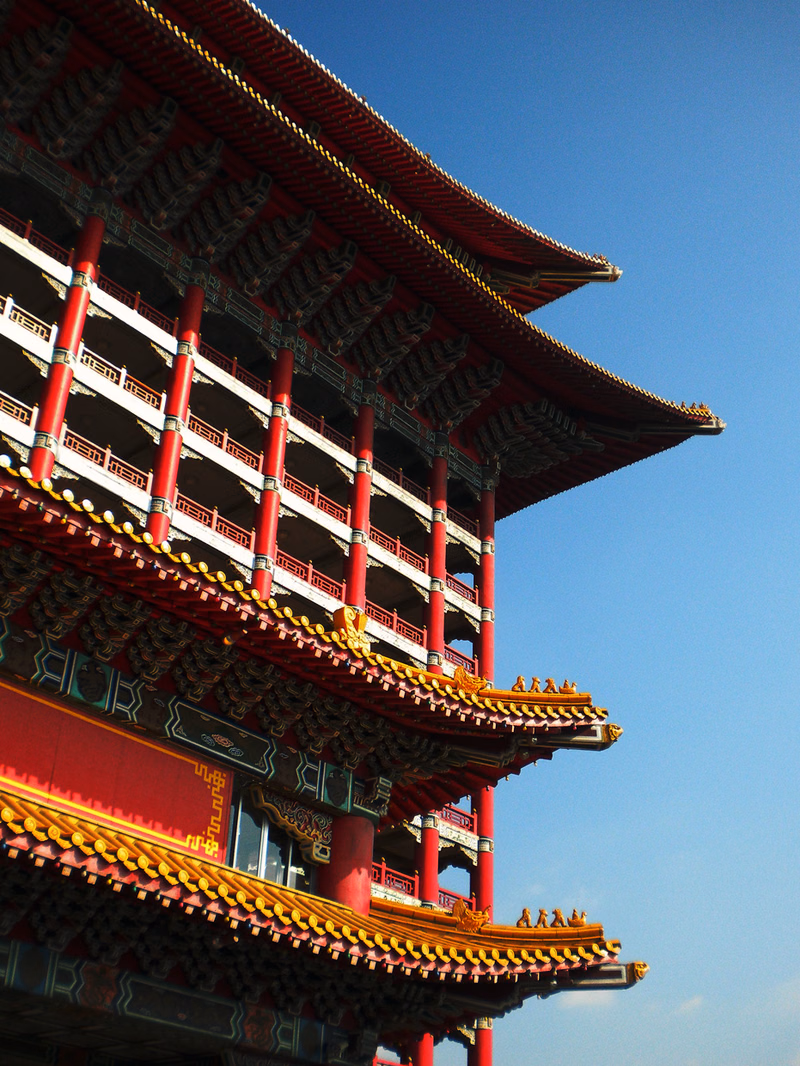 A multi-tiered traditional Chinese pagoda with a prominent red roof stands against a clear blue sky.