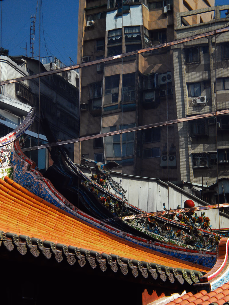 A vibrant, colorful roof against a backdrop of a modern, densely-packed building, with a clear blue sky above.