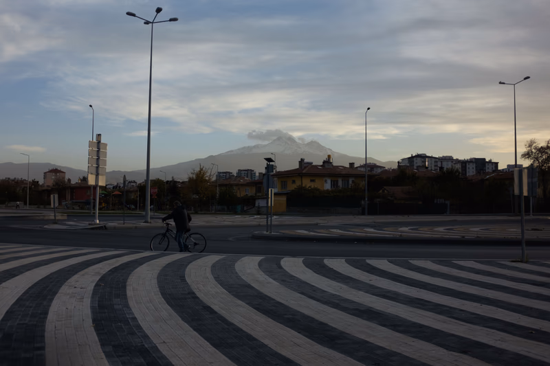A cyclist rides through a city with a mountain in the background.