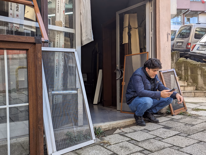 A man crouching outside a store, examining a mobile phone.