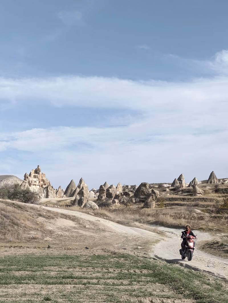 A motorcyclist rides through a rugged landscape with unique rock formations in the background.