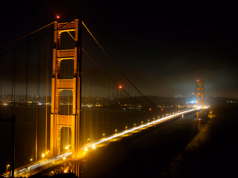 The illuminated Golden Gate Bridge spans across the water at night, with city lights visible in the background.