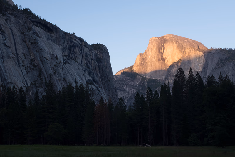 A photograph of a mountain with a forest in the foreground and a rock formation in the background.