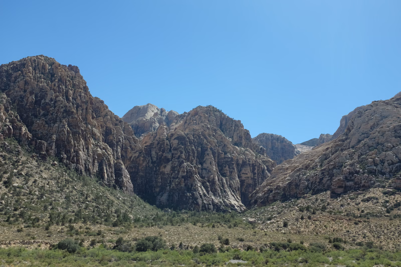 A view of rugged, rocky mountains and canyons under a clear, bright blue sky in a desert landscape.