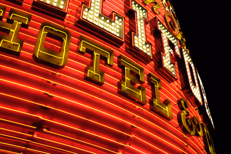 A close-up view of a brightly lit, curved hotel sign displaying the text "HOTEL" in large, glowing letters against a dark background.