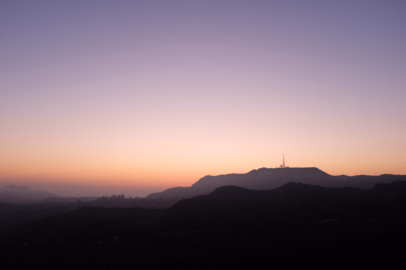 A serene sunset over rolling mountains, with a faint transmission tower visible on the distant ridge.