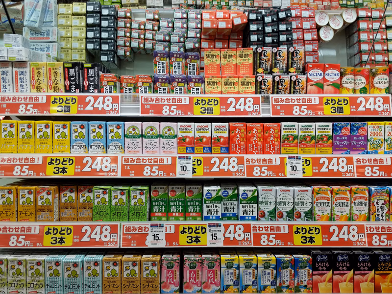A large display of various packaged snacks, chips, and candy bars, with visible pricing like "248円" and "85円" on the shelves.